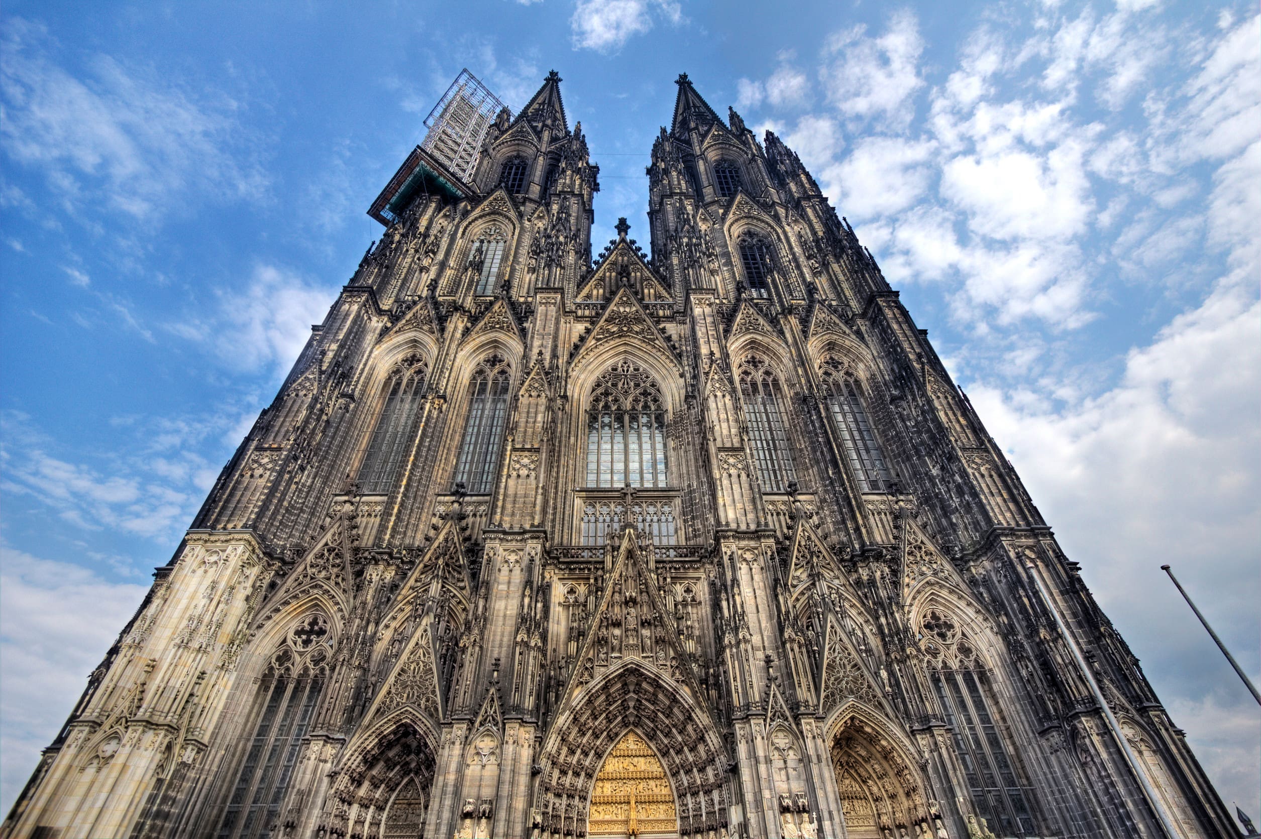 一張以極低角度仰拍的宏偉照片，展示了德國科隆大教堂 (Cologne Cathedral) 令人敬畏的西立面（正面）。